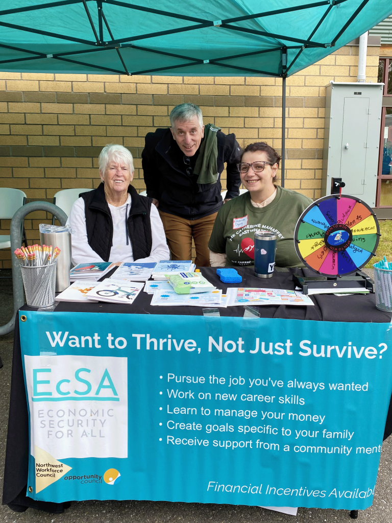 Three people sit or stand behind an info table with a banner that says "Want to thrive, not just survive?" and a logo that says "EcSA: Economic Security for All."