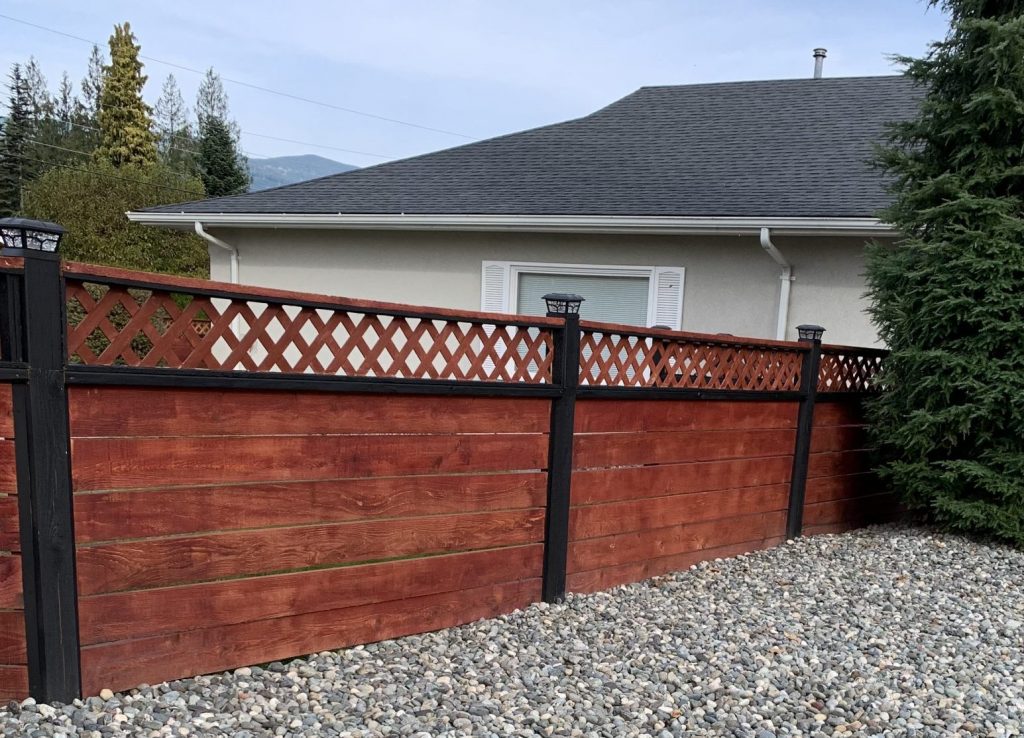 A fence with gravel on one side and a house on the other.