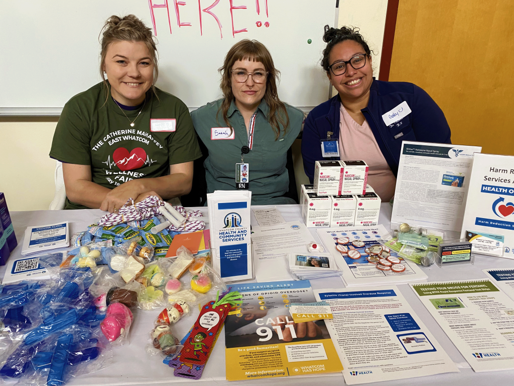 Three people sit at a table full of swag and resources.