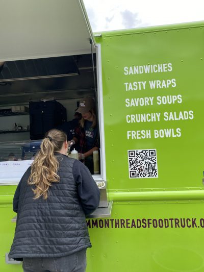 A woman stands in front of the bright green Common Threads Food Truck, waiting for her delicious meal.