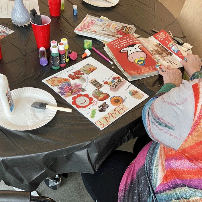 A person sits at a circular table poring over a magazine, next to the vibrant collage they're creating.