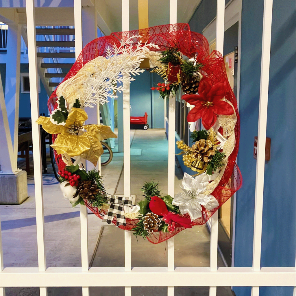 A vibrant wreath with flowers, berries, and pine branches on it hangs on a gate.